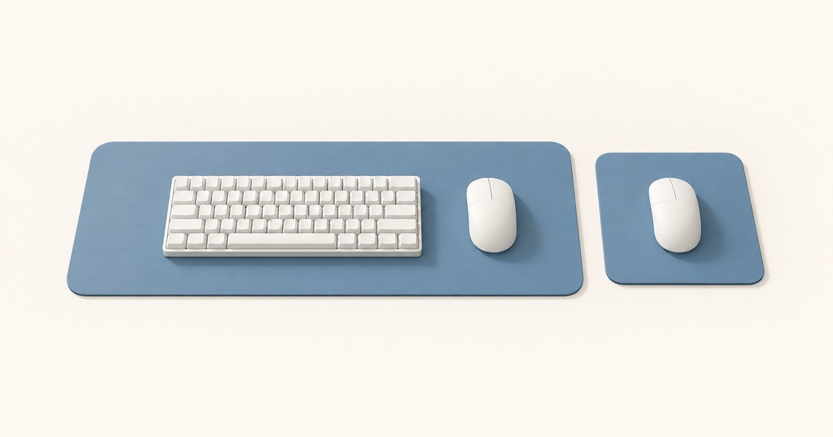 A wide blue desk mat holding a white compact keyboard and mouse sits beside a small square blue mouse pad with a second white mouse on a cream background.