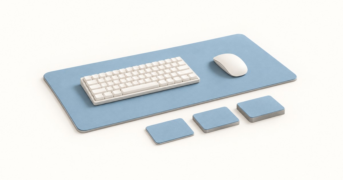 Blue desk mat holding a white compact keyboard and mouse, with three small square samples of increasing thickness lined up in front on a white surface
